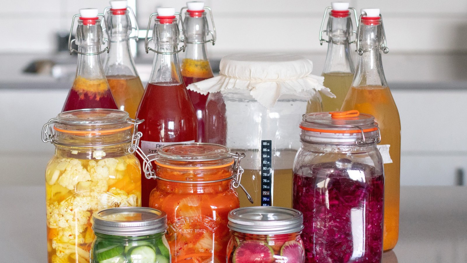 Botellas de tapón mecánico con refrescos fermentados junto a tarros de fermentos vegetales