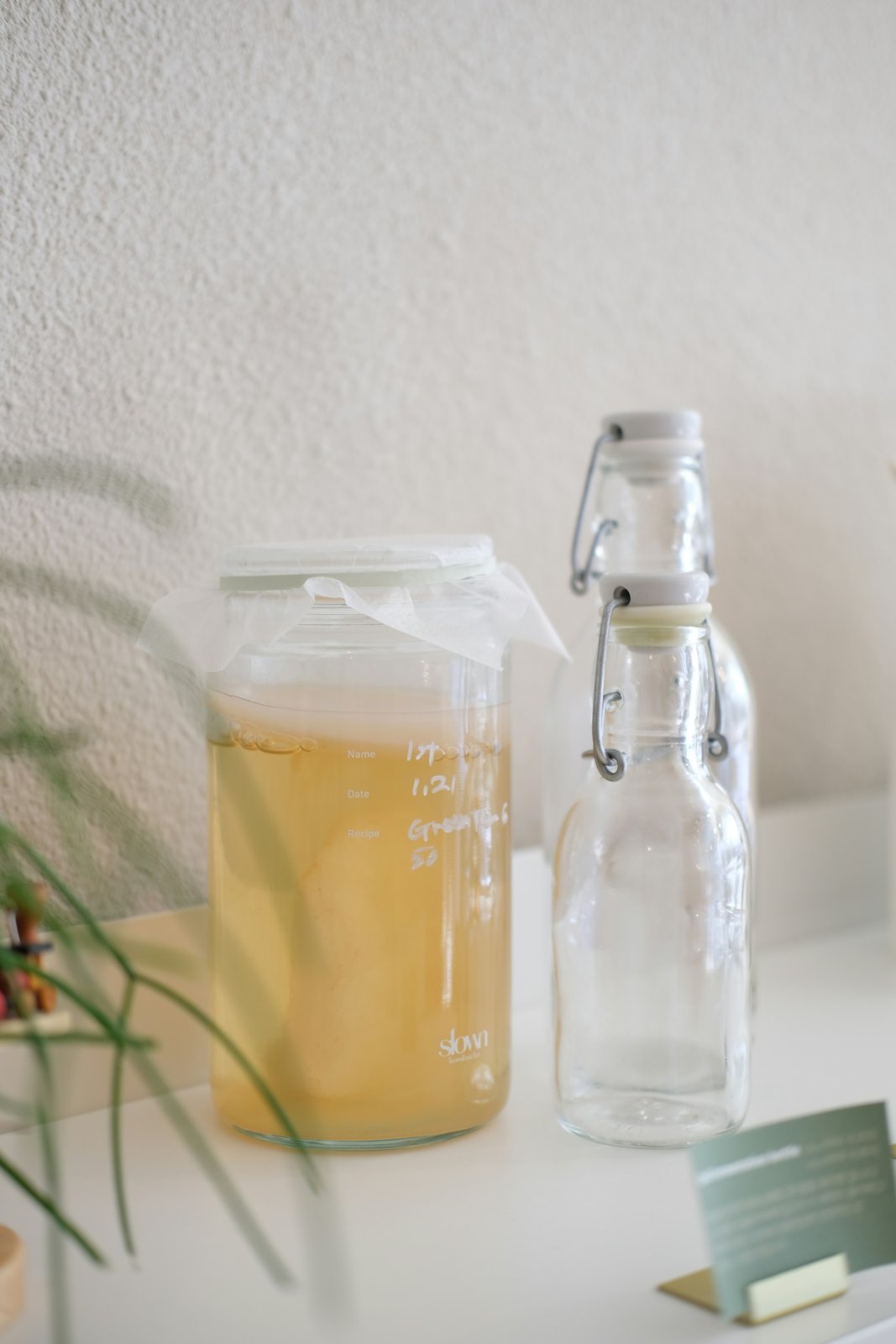 Tarro de primera fermentación tapado con un paño junto a dos botellas con tapón mecánico